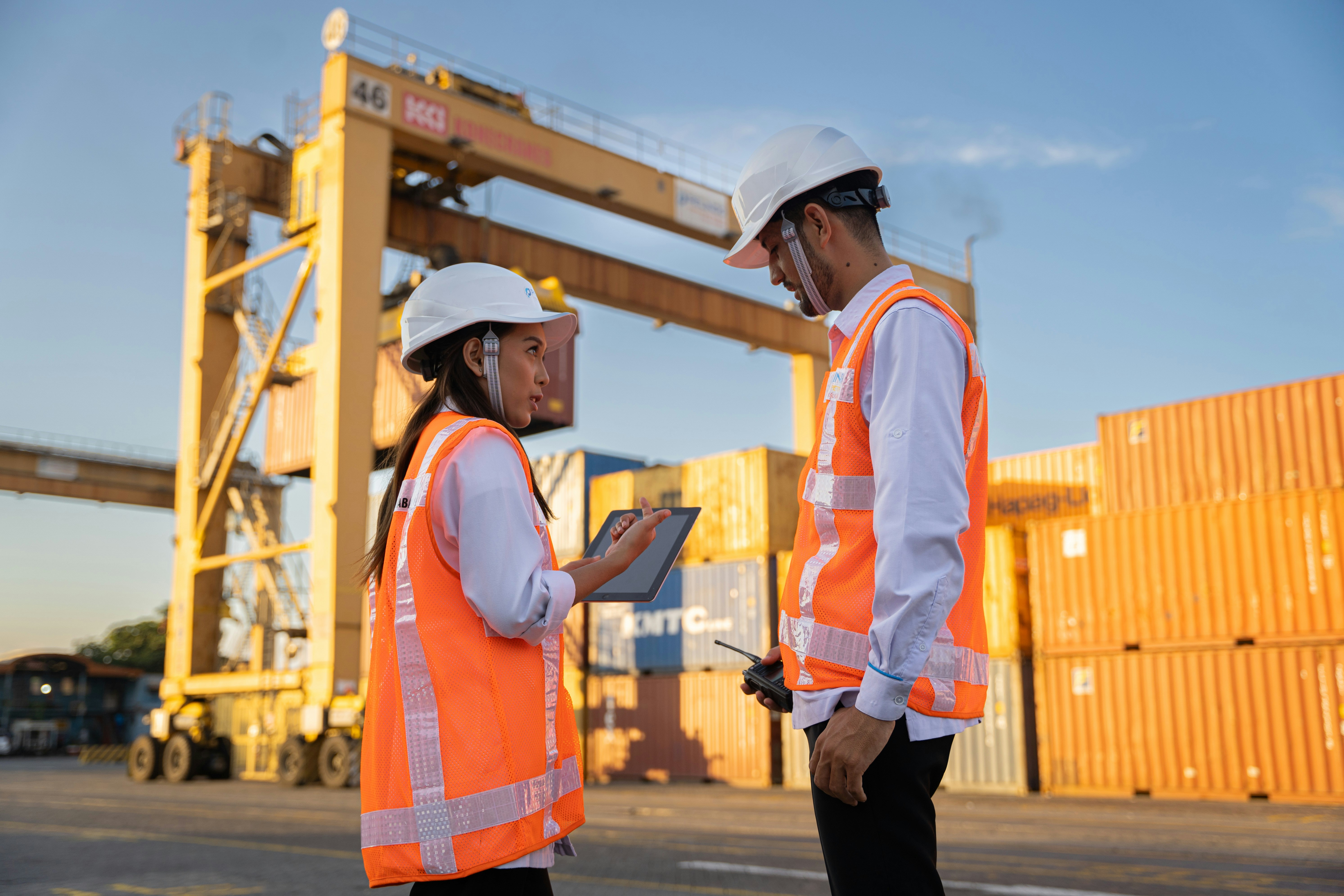 Two logistics workers in safety vests reviewing plans at a container yard